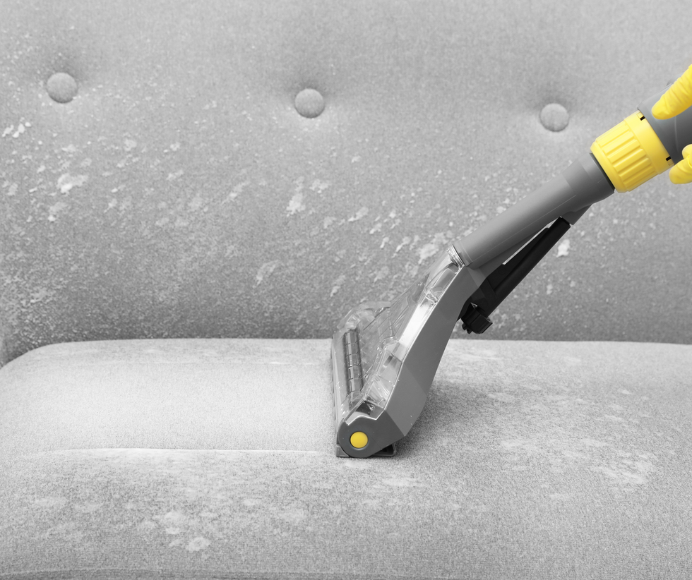 Vacuum nozzle cleaning a gray upholstered sofa