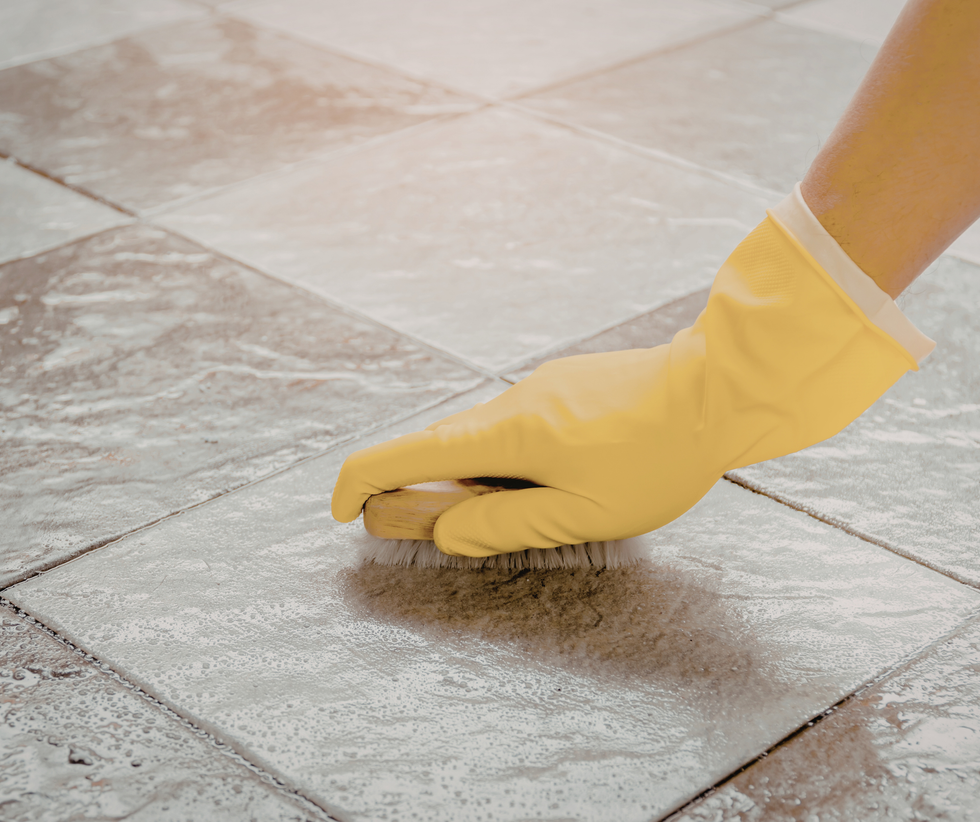 Yellow-gloved hand scrubbing a tiled floor with a sponge, cleaning grout.