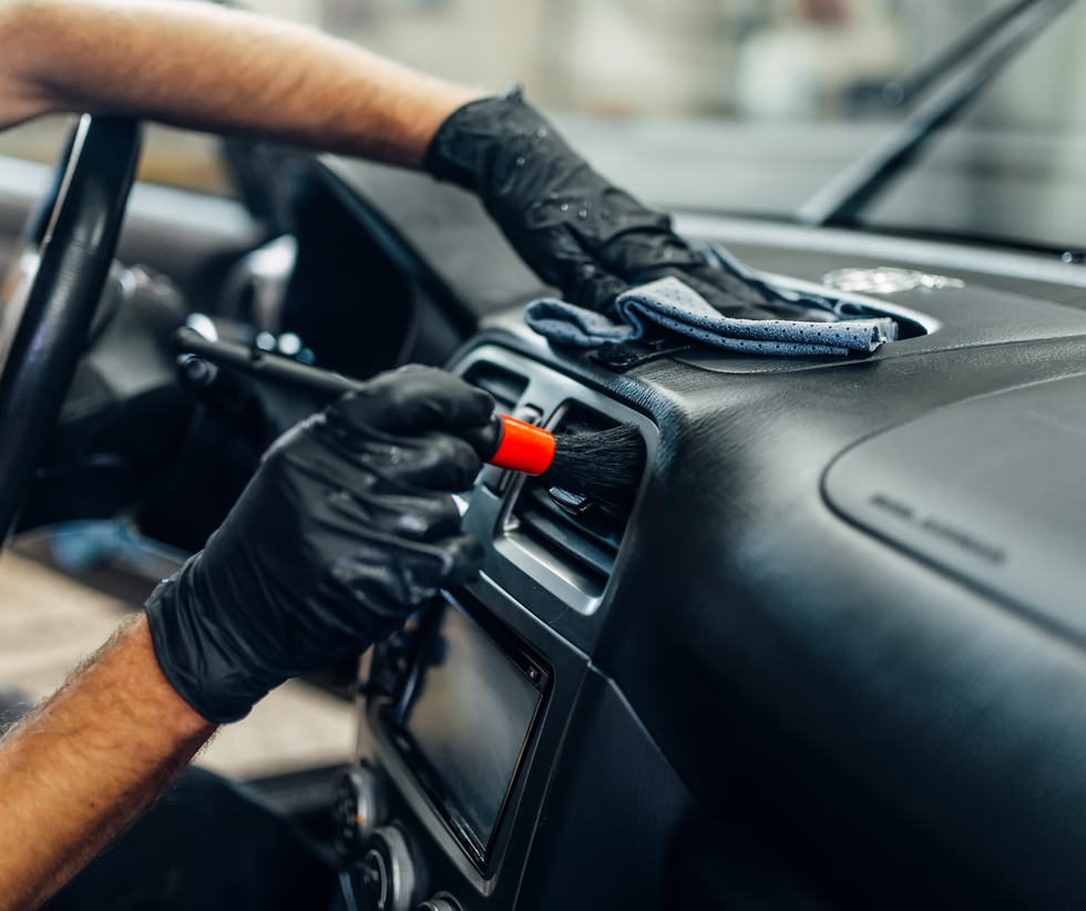 Gloved hands detailing a car dashboard with a microfiber cloth and spray bottle