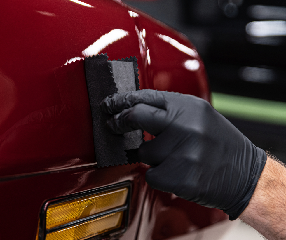 Gloved hand polishing a red car’s front fender near the headlight and turn signal