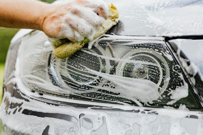 Hand washing a car windshield with a soapy sponge