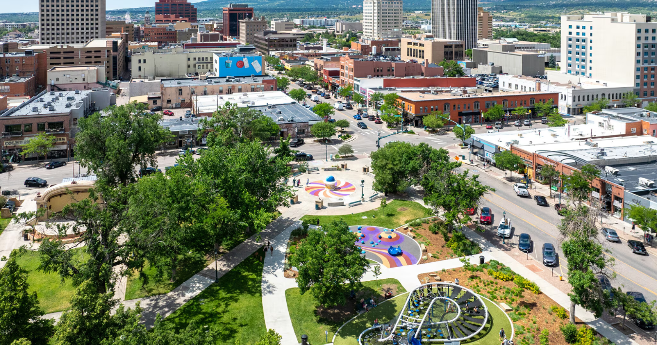 Aerial view of a city park with buildings and streets in the background on a sunny day.
