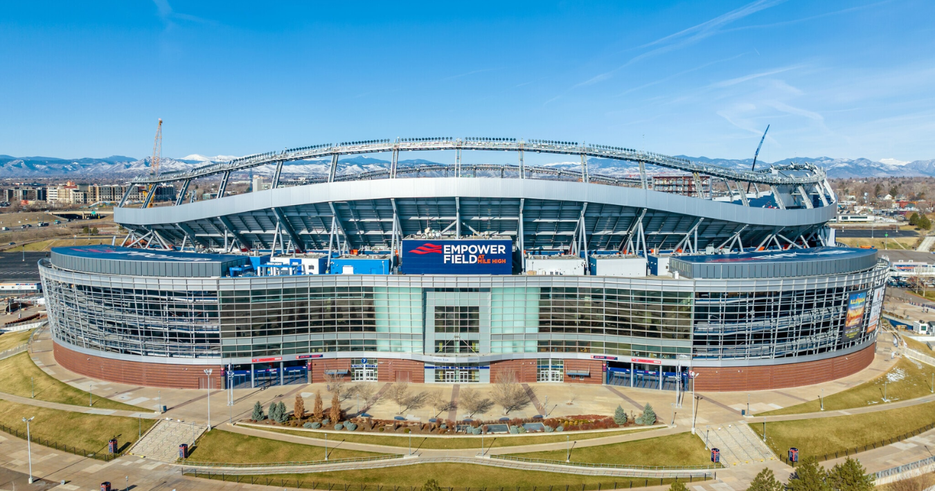 Empower Field at Mile High Stadium with mountains in the background, clear blue sky.