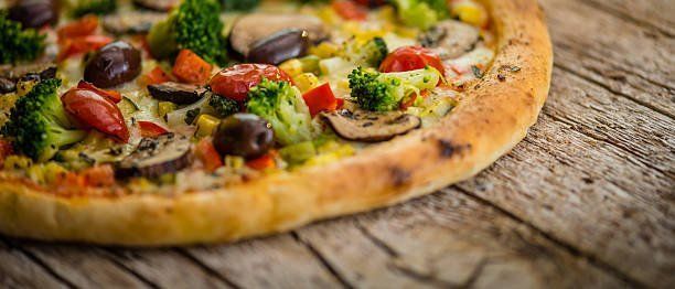 A pizza with broccoli , mushrooms , tomatoes and olives on a wooden table.