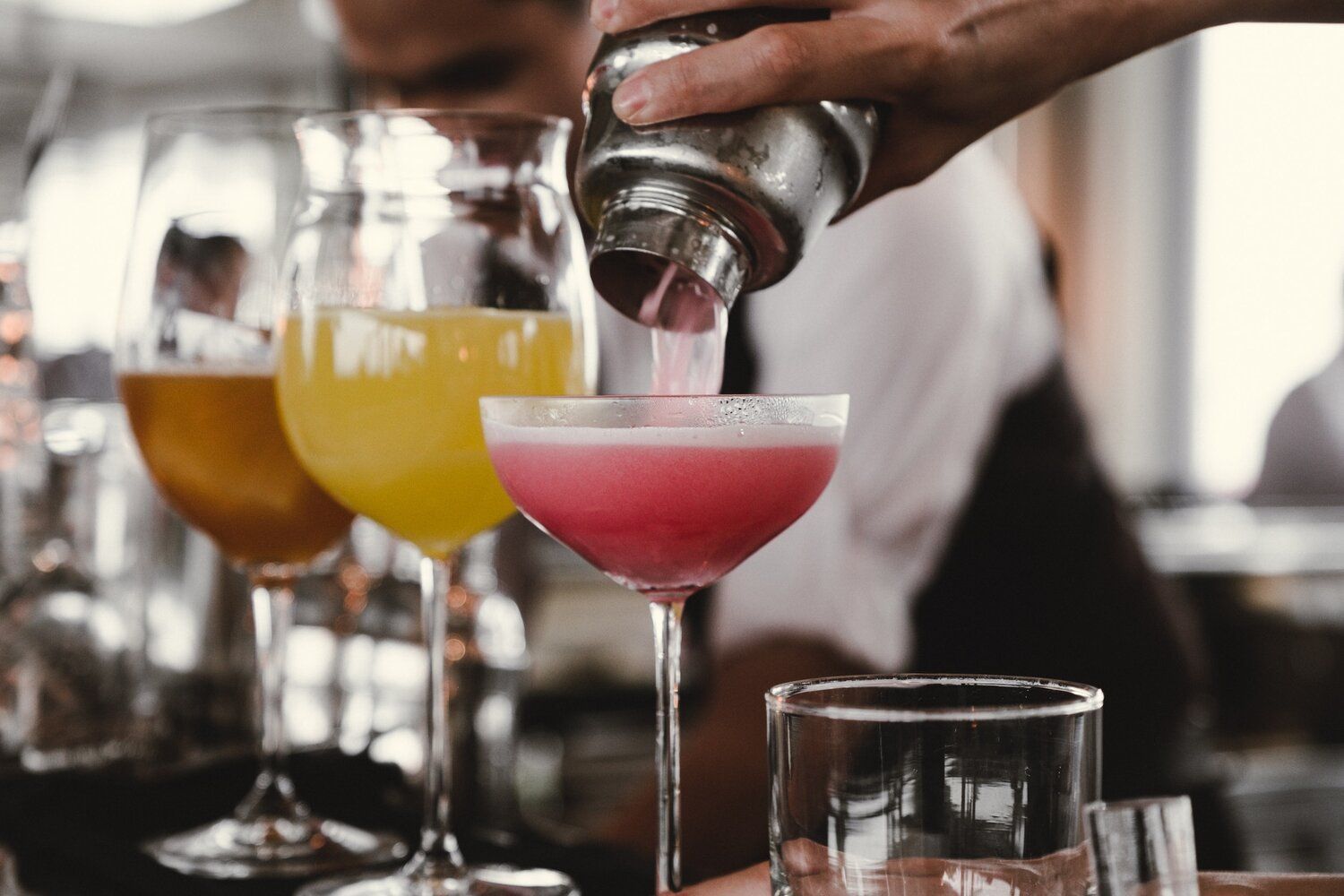 A bartender is pouring a cocktail into a martini glass.
