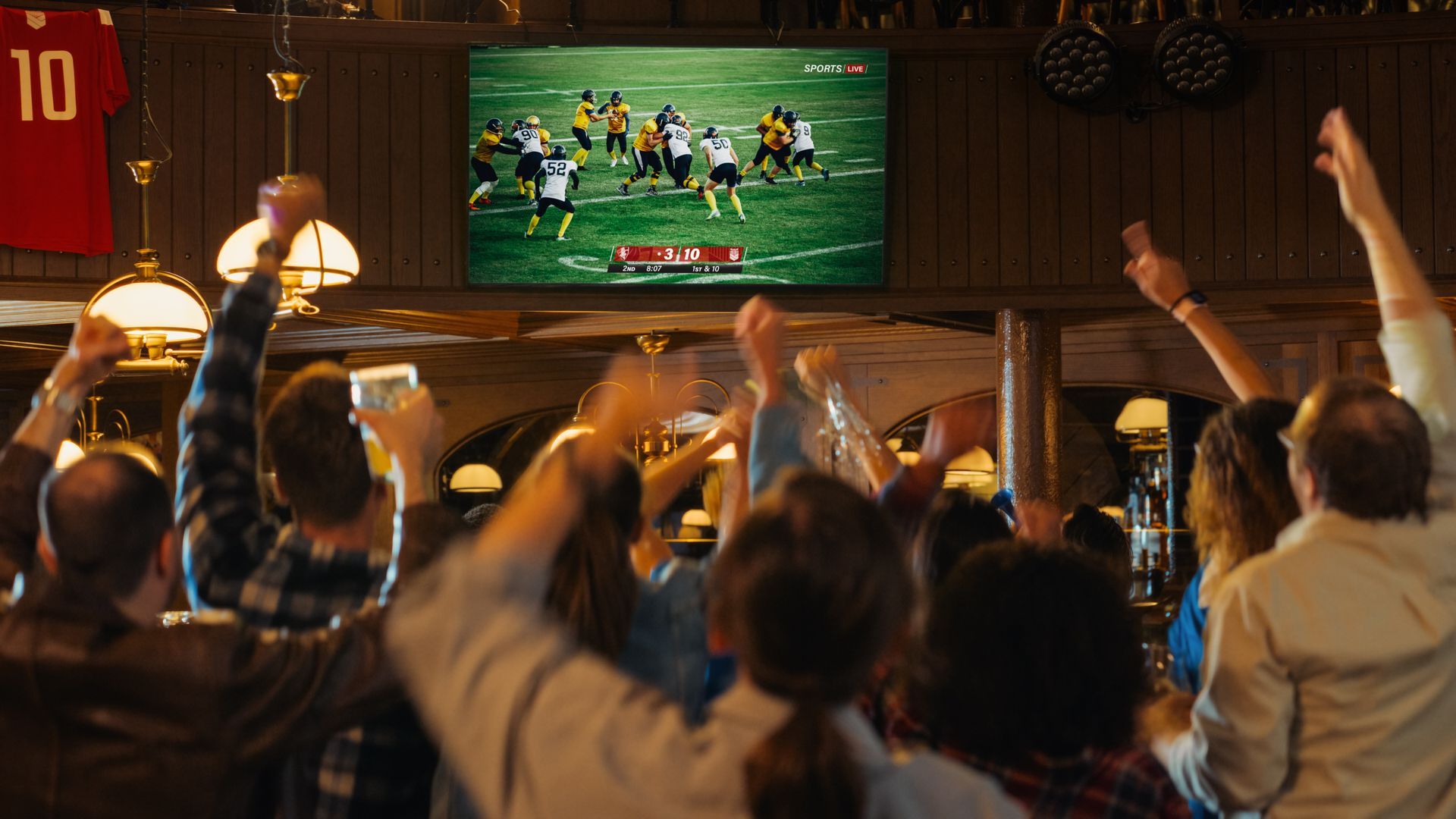 A group of people are watching a football game on a television in a bar.