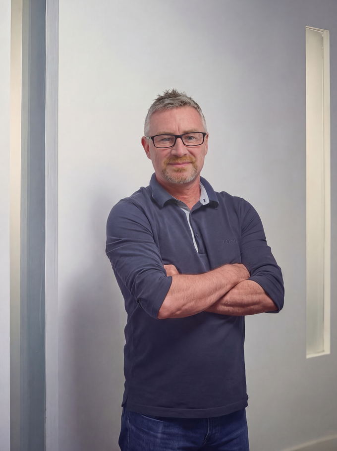 Man in glasses with arms crossed, wearing a navy polo shirt, standing against a white wall. Nick Aldrich, CEO of ACI Studios.