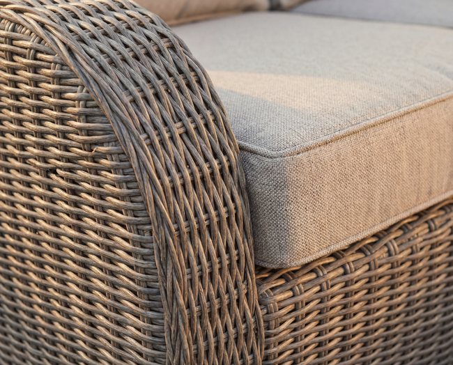 Close-up of a wicker chair arm and cushion. Light beige weave, off-white cushion.