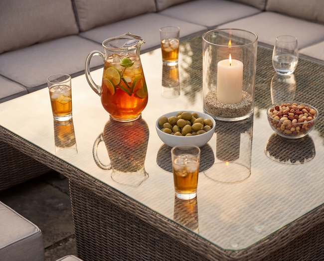 Group of people laughing around outdoor seating with a fire pit in a sunny garden.
