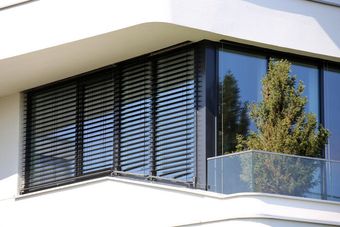 Modern Building Balcony with Glass Railing, Black Louvered Shutters, and Trees Visible Through the Window — Glass Installations & Repairs in Gympie, QLD
