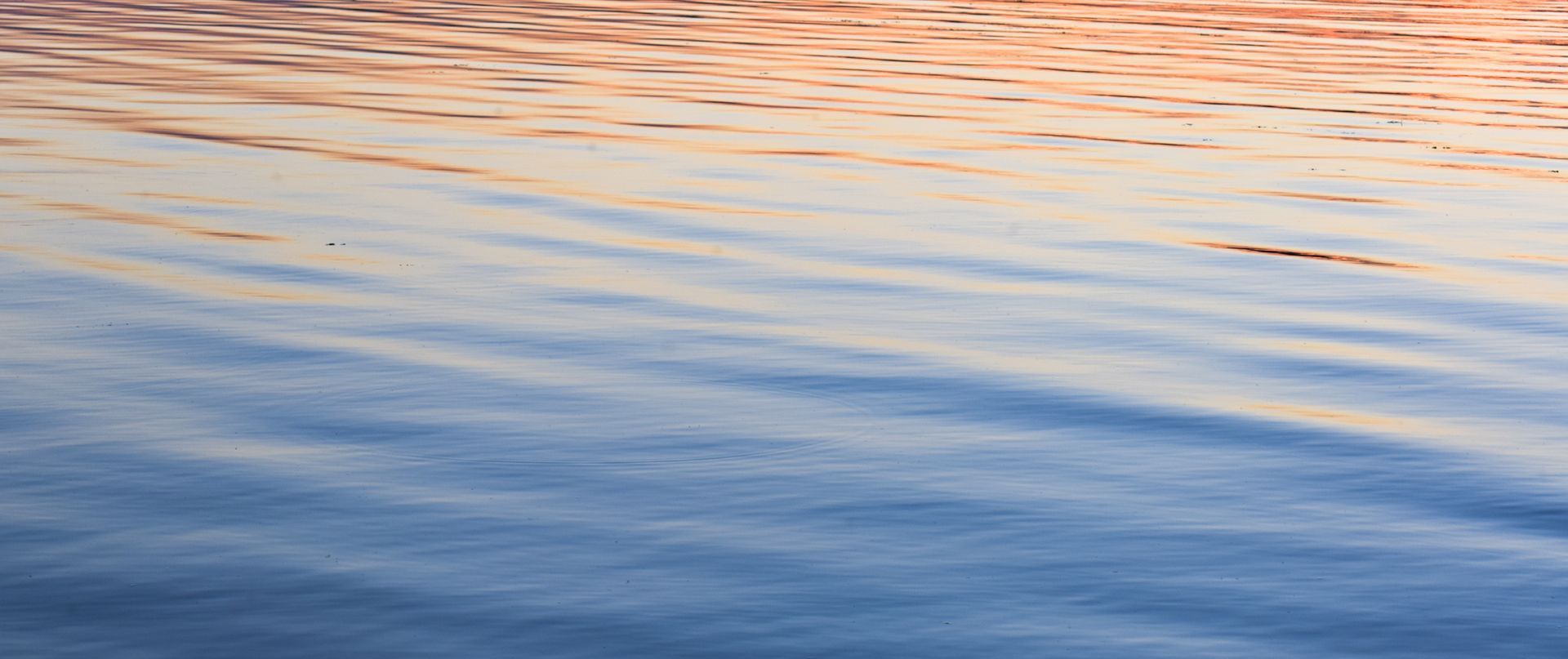 A close up of a body of water with waves and a sunset in the background.