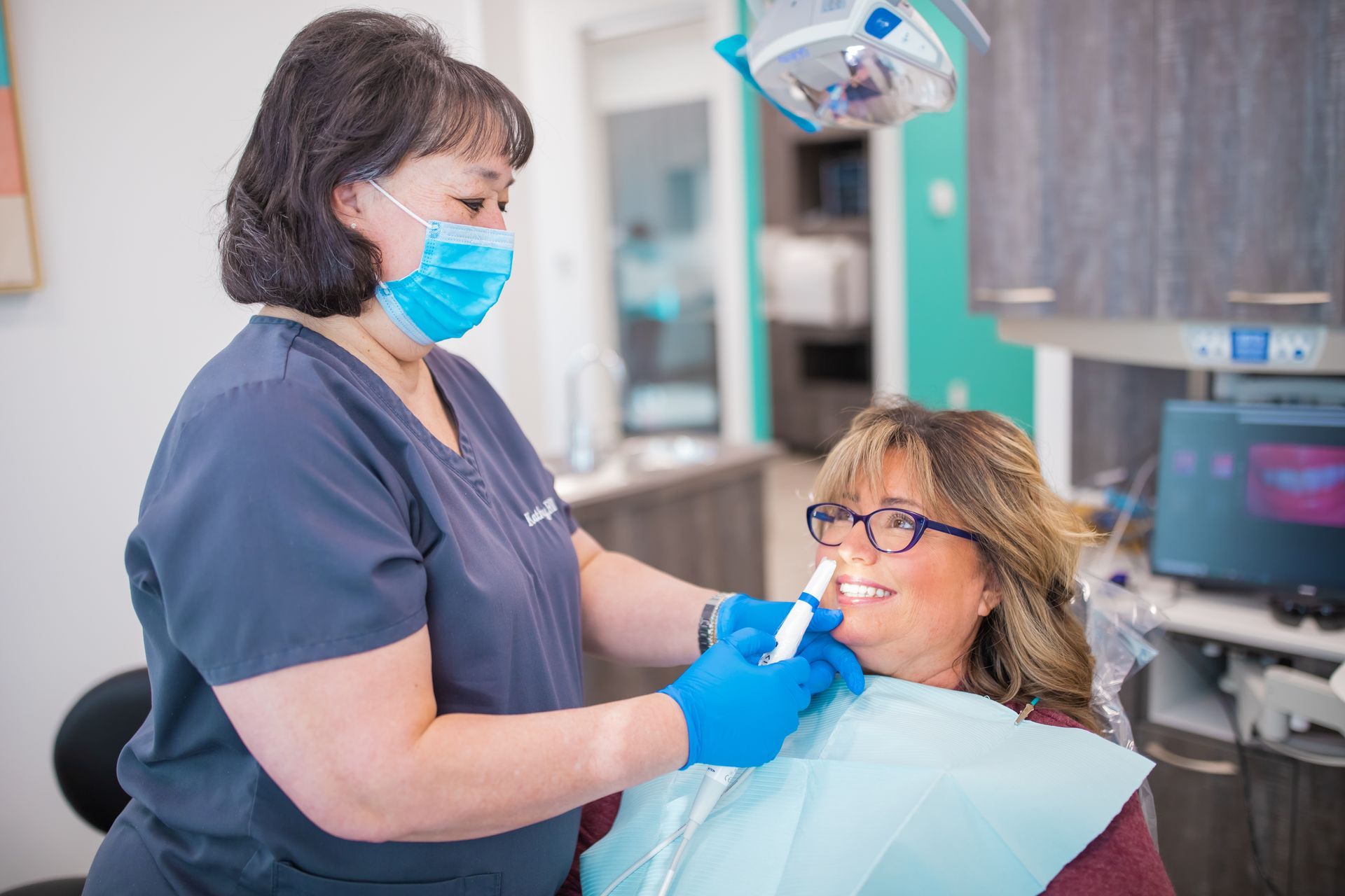 Dental hygienist examining a patient's teeth. Bright office with dental equipment.
