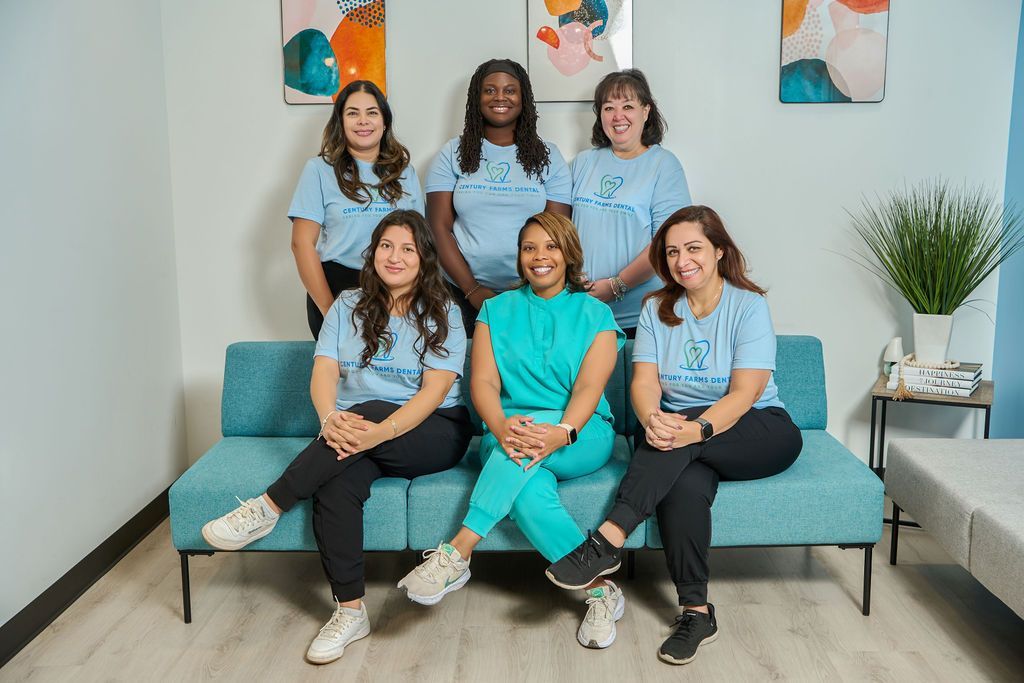 Group of women posing together, some seated on a teal couch, wearing blue shirts, in a room with art on the wall.