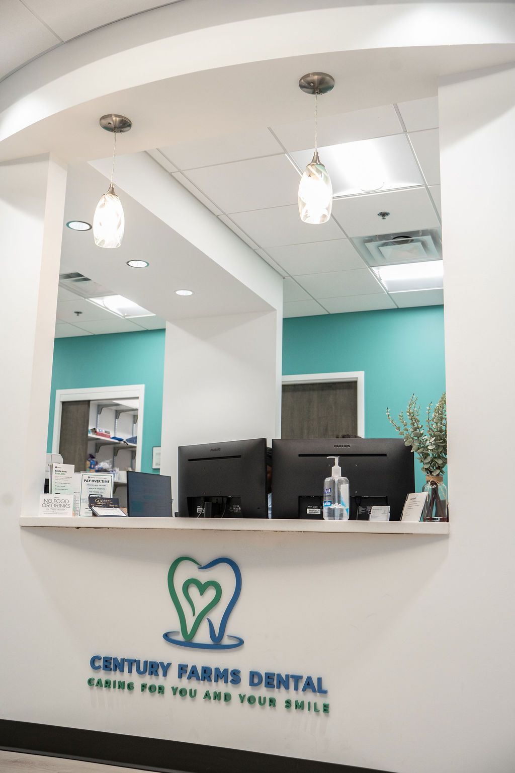 Reception area for Century Farms Dental. Turquoise wall, two computer monitors, logo with heart in tooth.