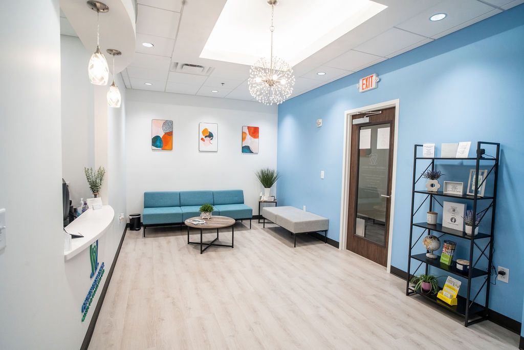 Bright, modern waiting room with turquoise sofa, round coffee table, and blue walls. Black shelving unit on the right.