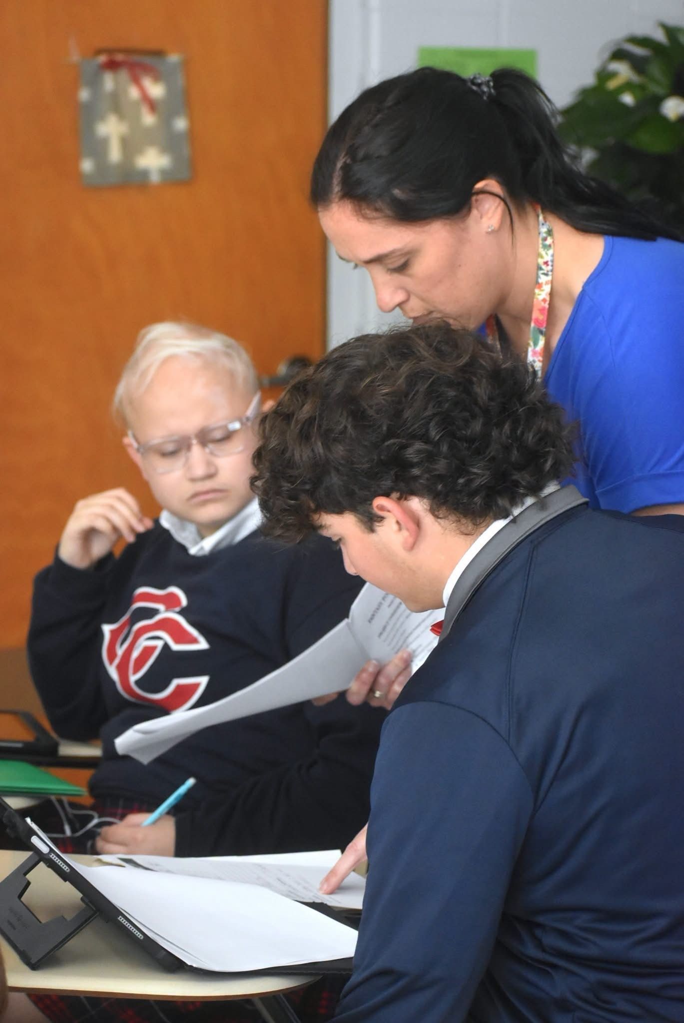 Three children are sitting at a table in a classroom and smiling for the camera