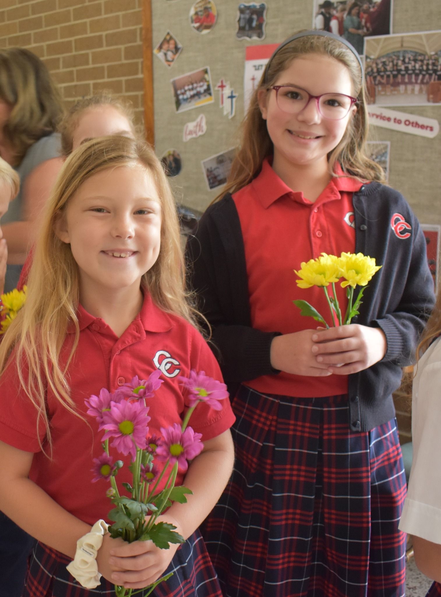 Two girls in school uniforms are holding flowers and smiling