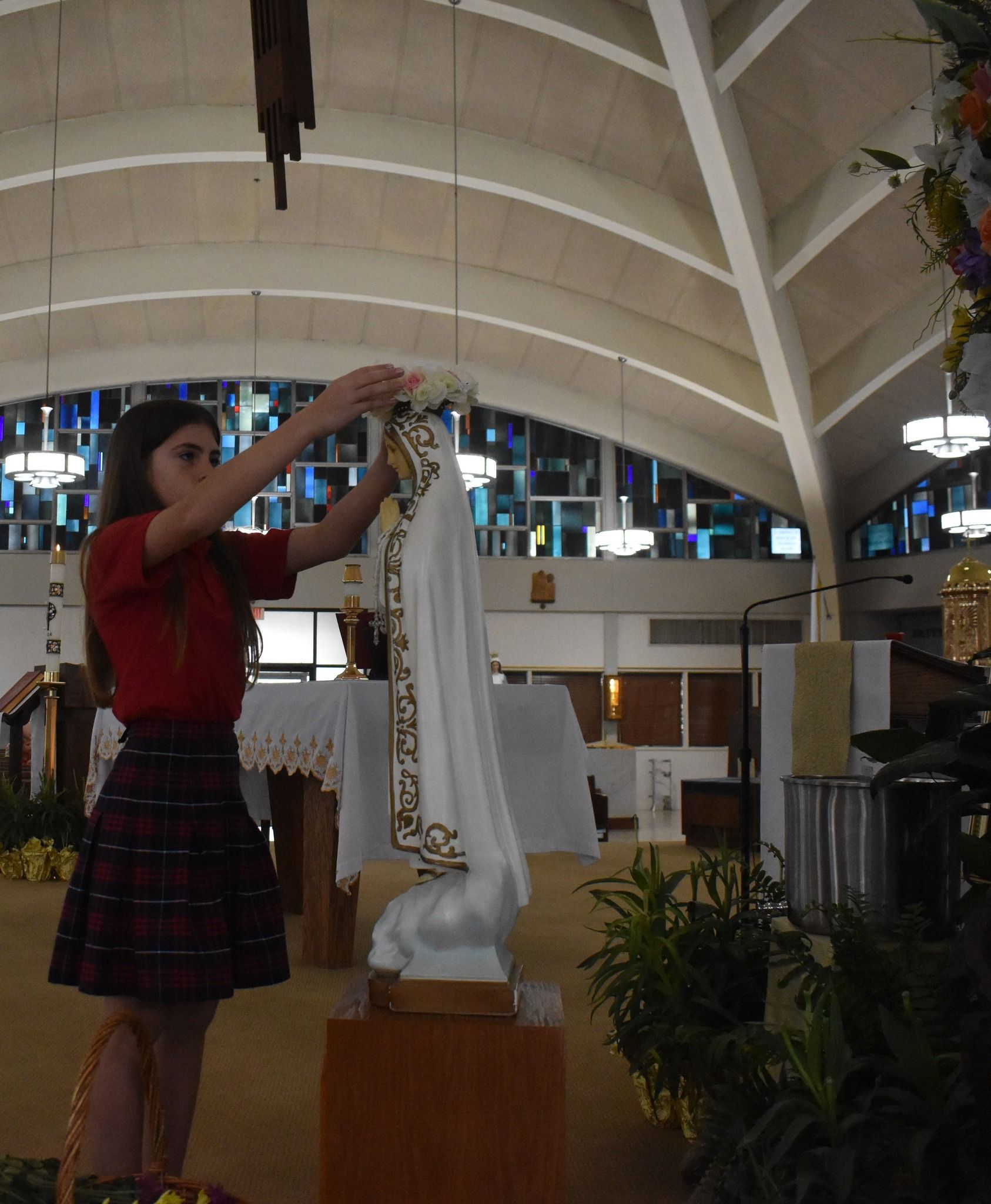 A girl in a red shirt and plaid skirt holds a statue in a church