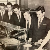 A group of men in suits and ties are standing at a counter in a restaurant.