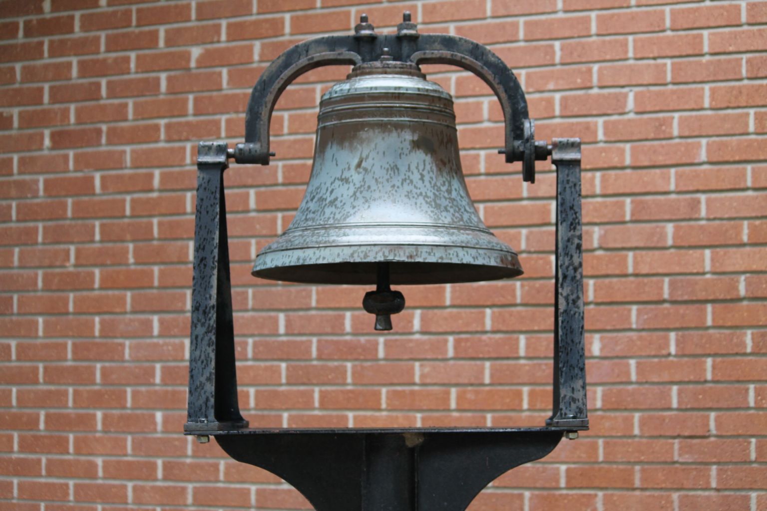 A large bell is hanging from a metal frame in front of a brick wall
