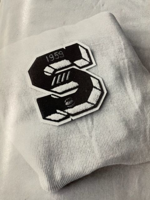 A black and white photo of a white shirt with the letter s on it