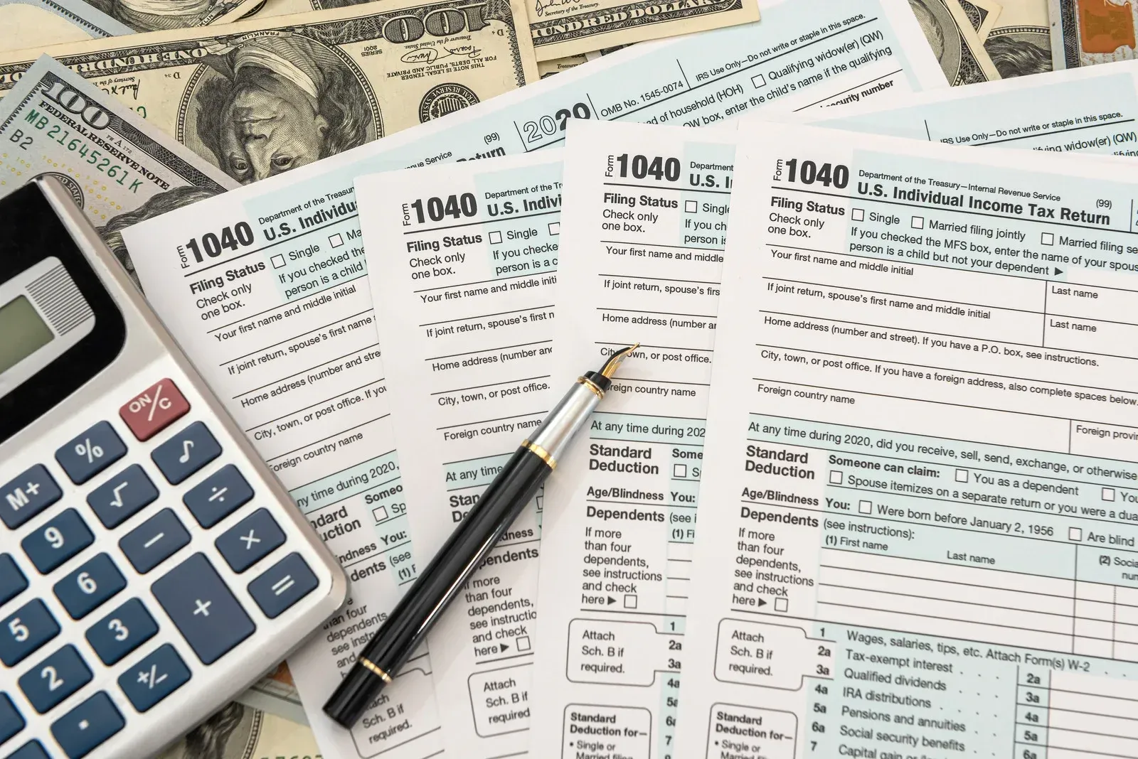 Tax forms, calculator, pen, and money on a desk.