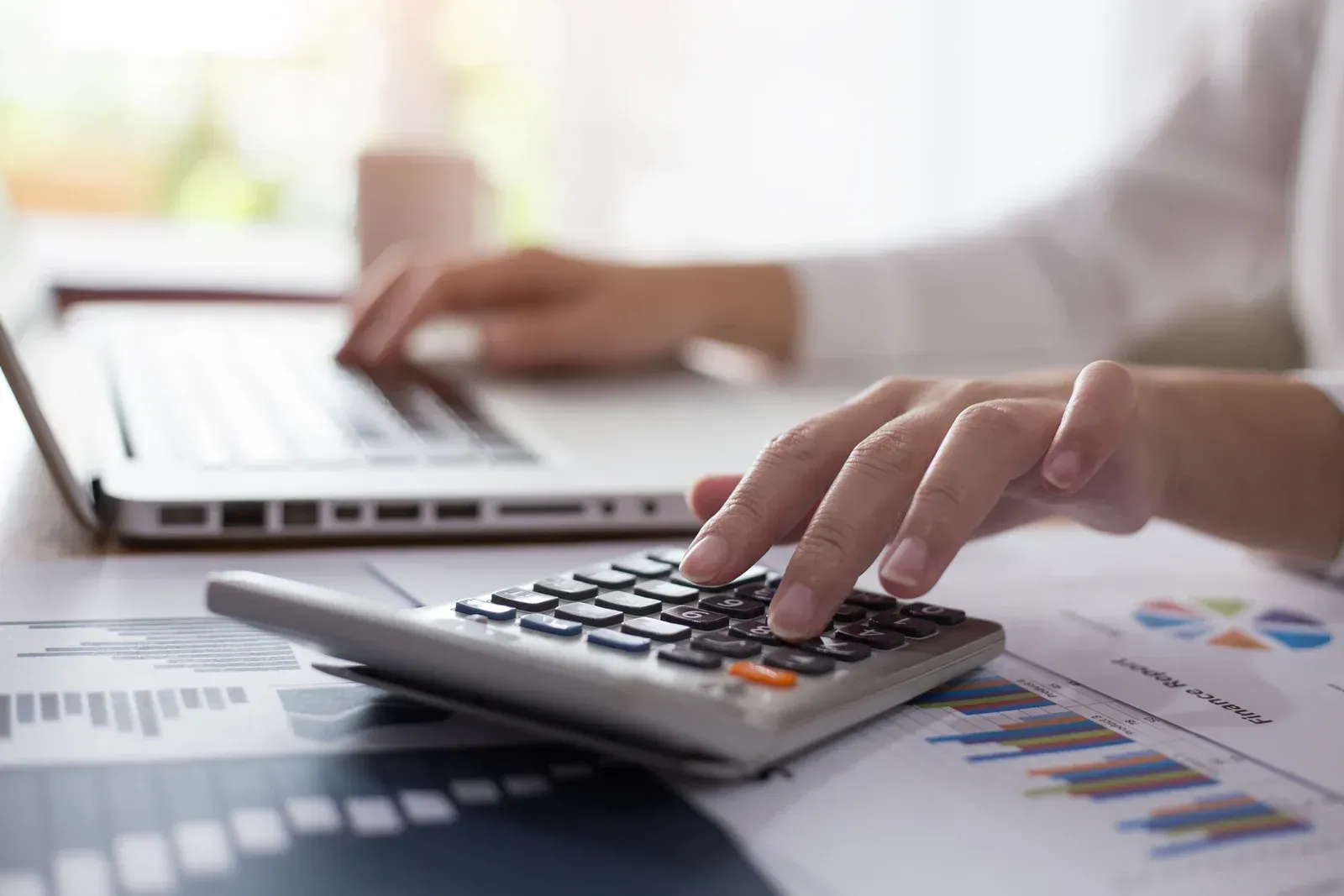Person using a calculator and laptop, working with financial documents.
