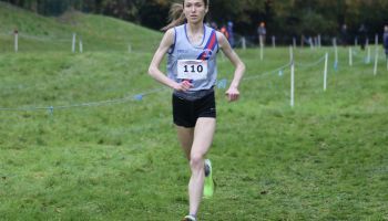 A woman is running on a grassy field in a cross country race.