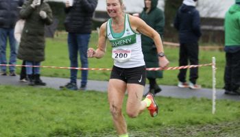 A woman is running in a cross country race in front of a crowd.