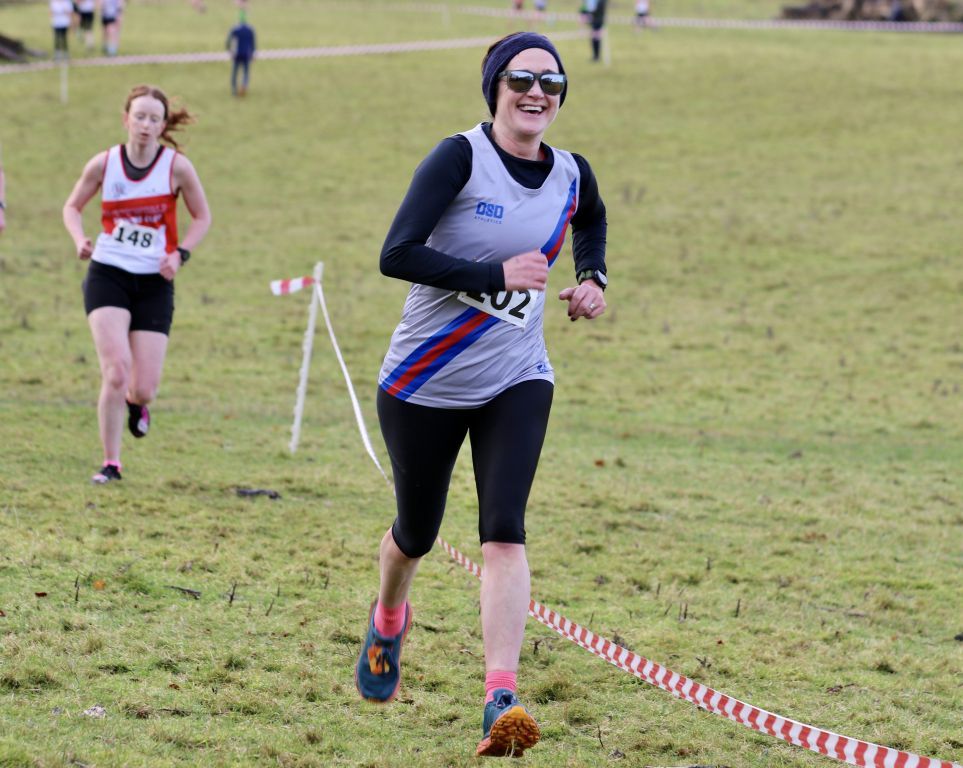 A woman is running in a cross country race in a field.