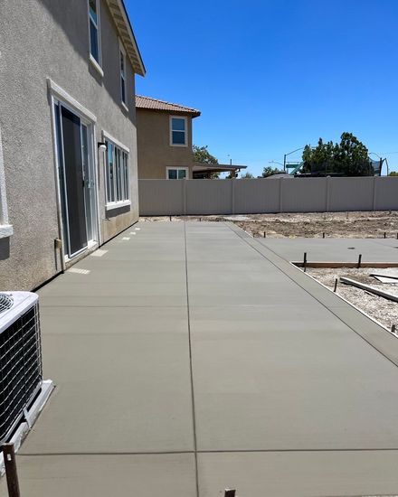 Newly poured concrete patio next to a two-story beige house under a bright blue sky.