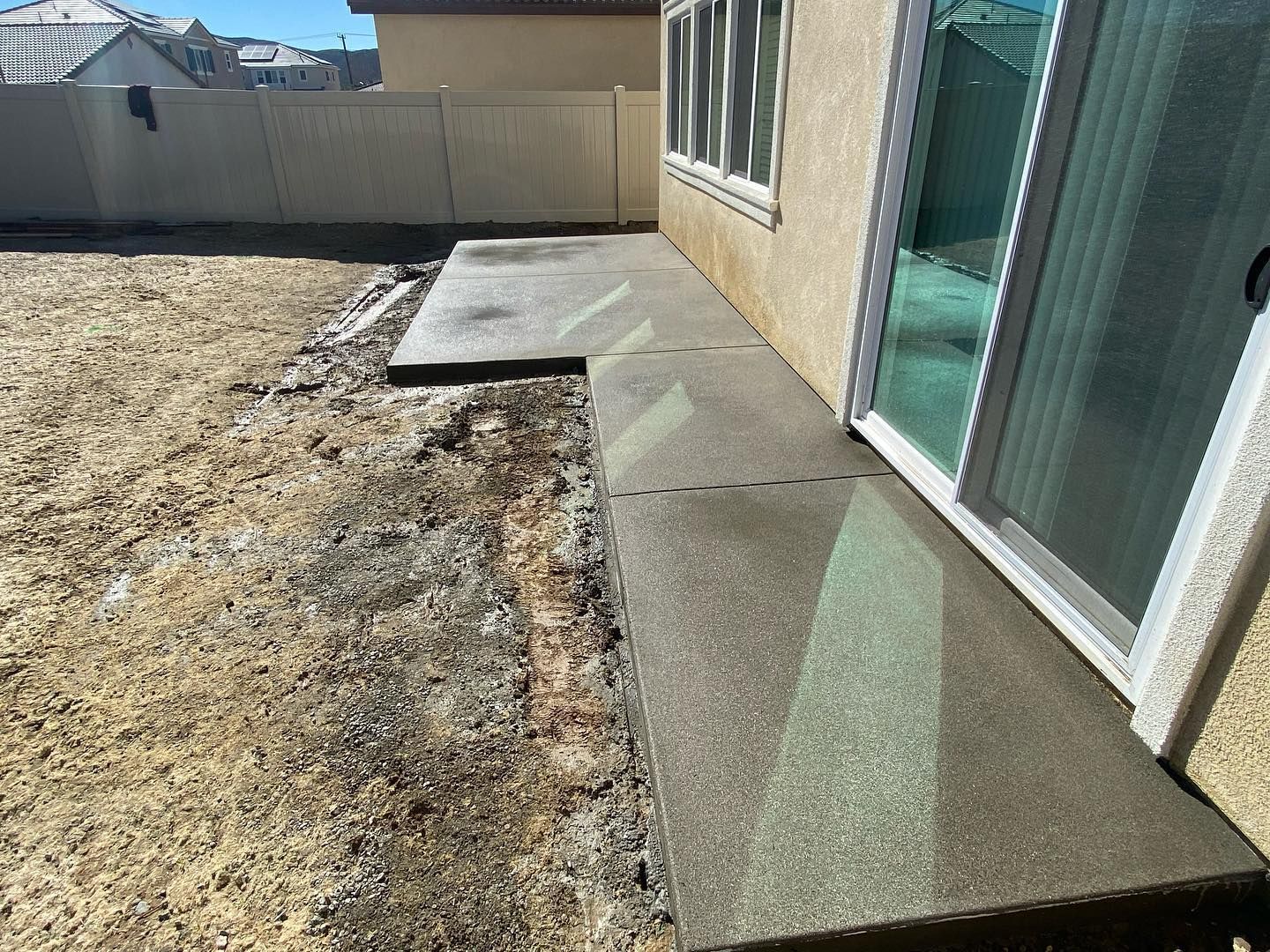 Concrete patio next to a house with a sliding glass door. The yard is dirt and grass.