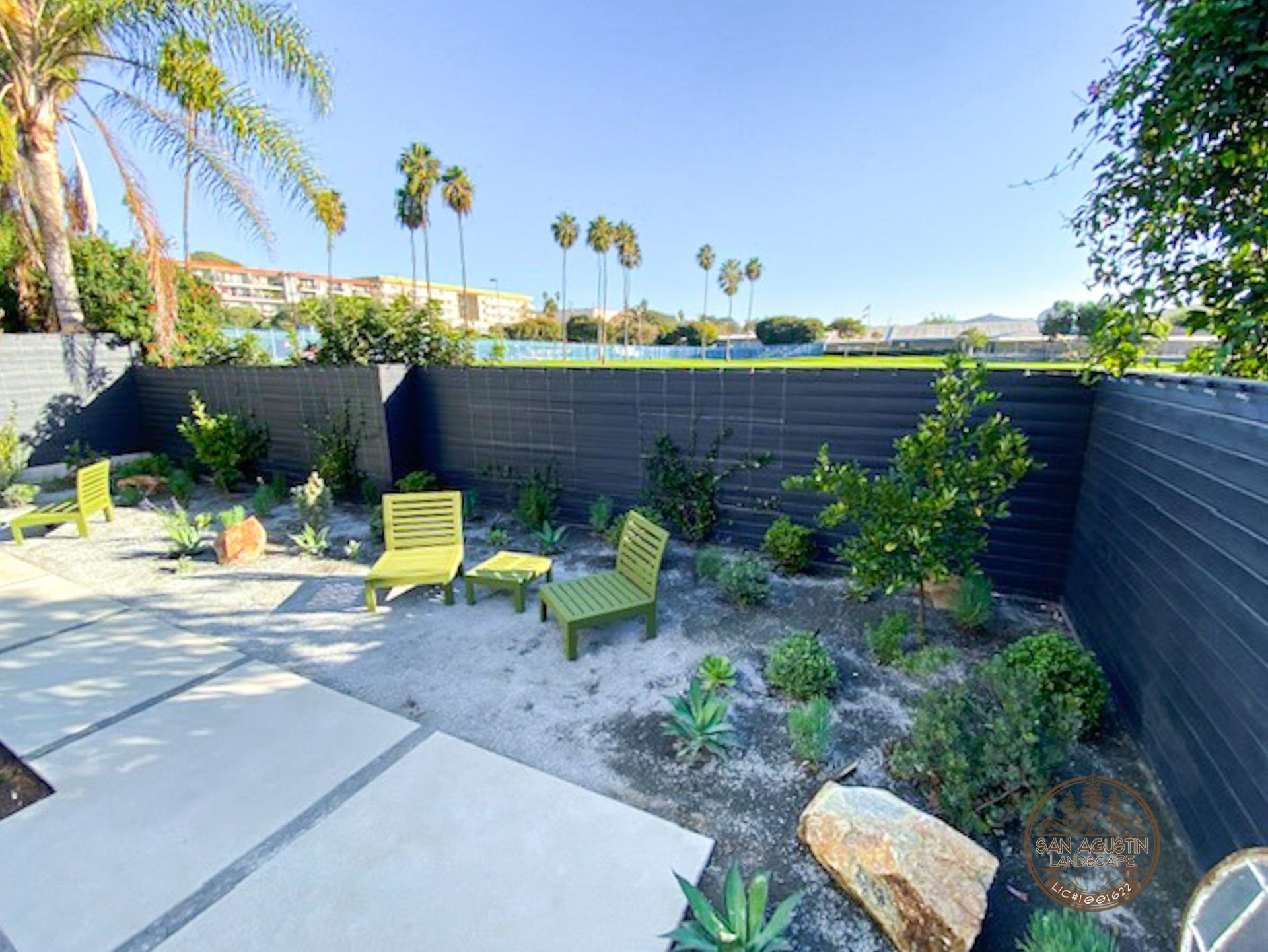Backyard with modern seating, landscaping, and a dark fence under a sunny sky.