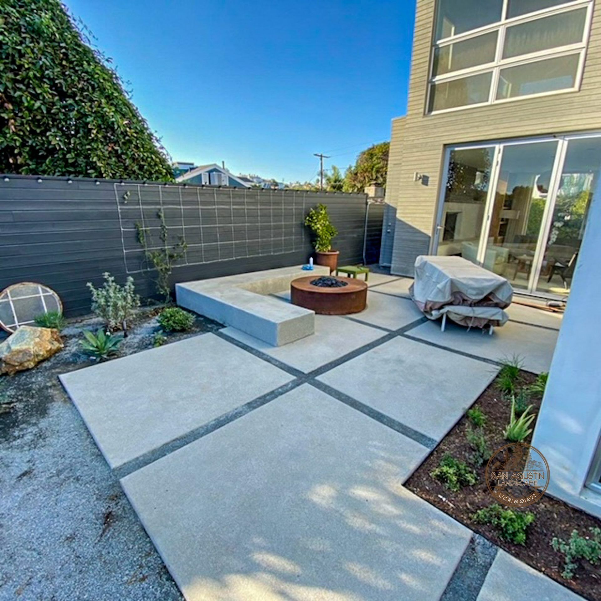 Modern outdoor patio with fire pit, concrete pavers, and gray wall.