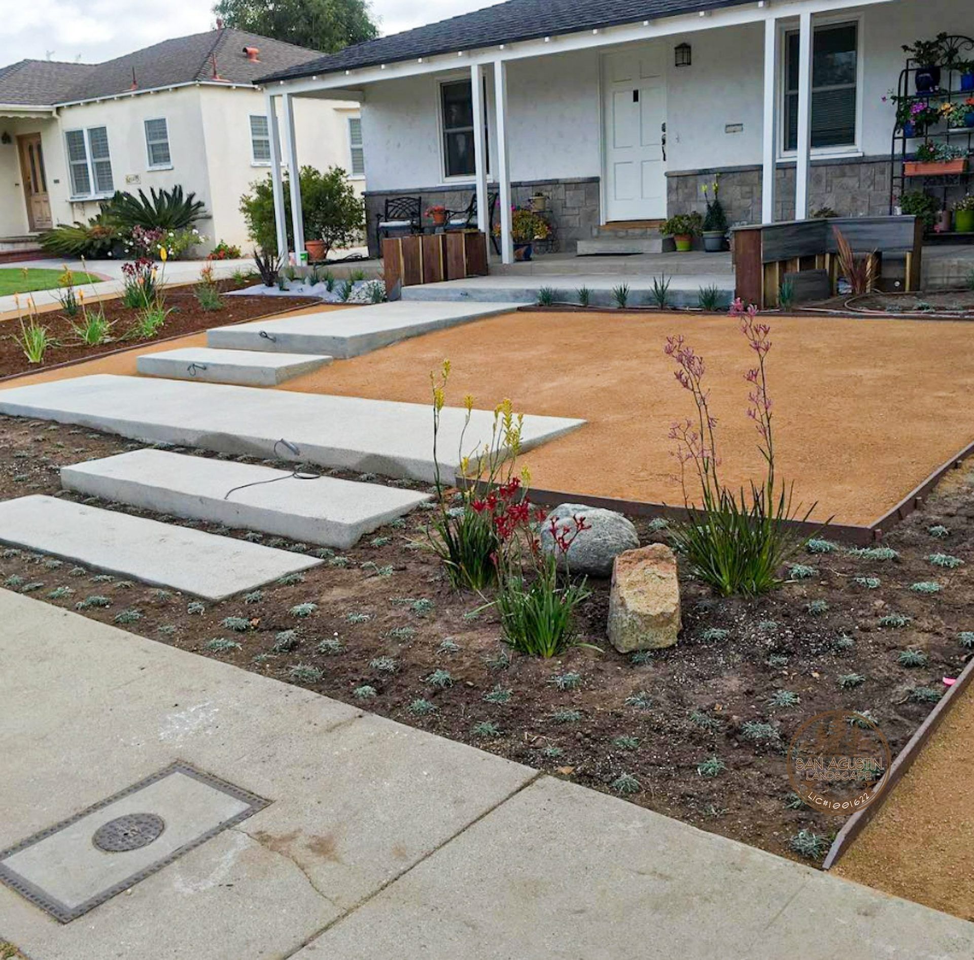Landscaped front yard with concrete steps, gravel, and plants leading to a white house with a porch.
