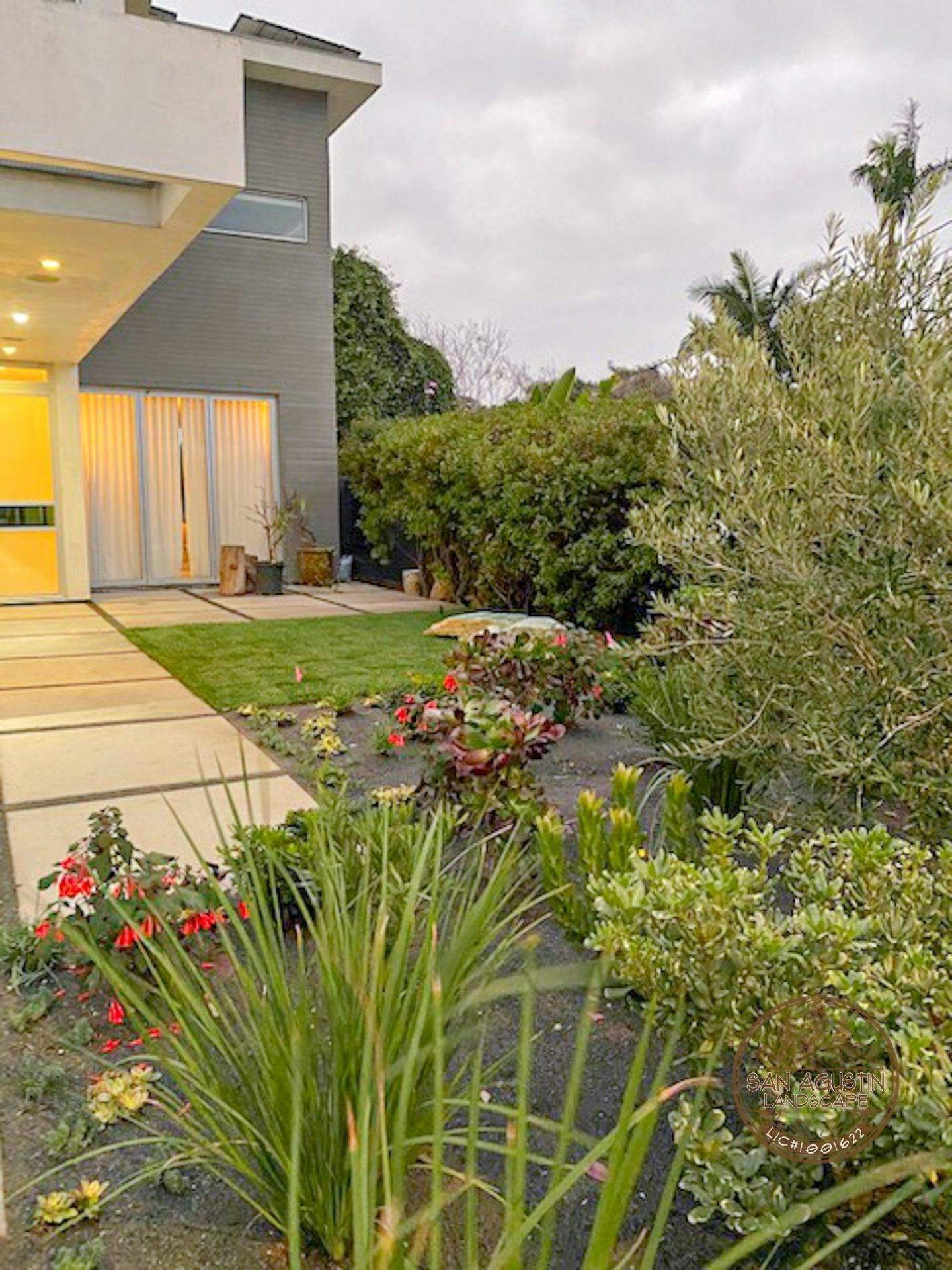 Front yard with landscaping and modern gray house. Cloudy sky.