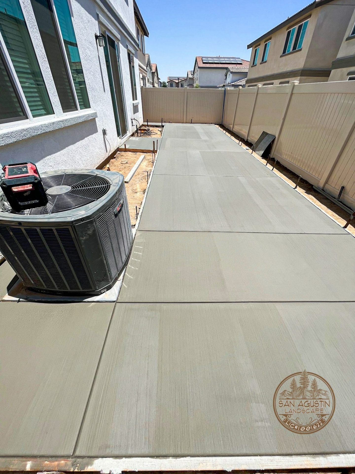 Freshly poured concrete patio beside a house, with an air conditioning unit visible.