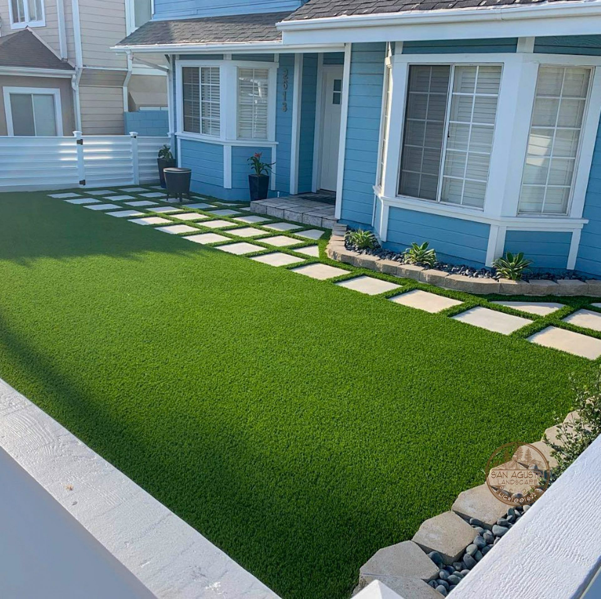 Blue house with a green lawn and stone pathway. White fence.