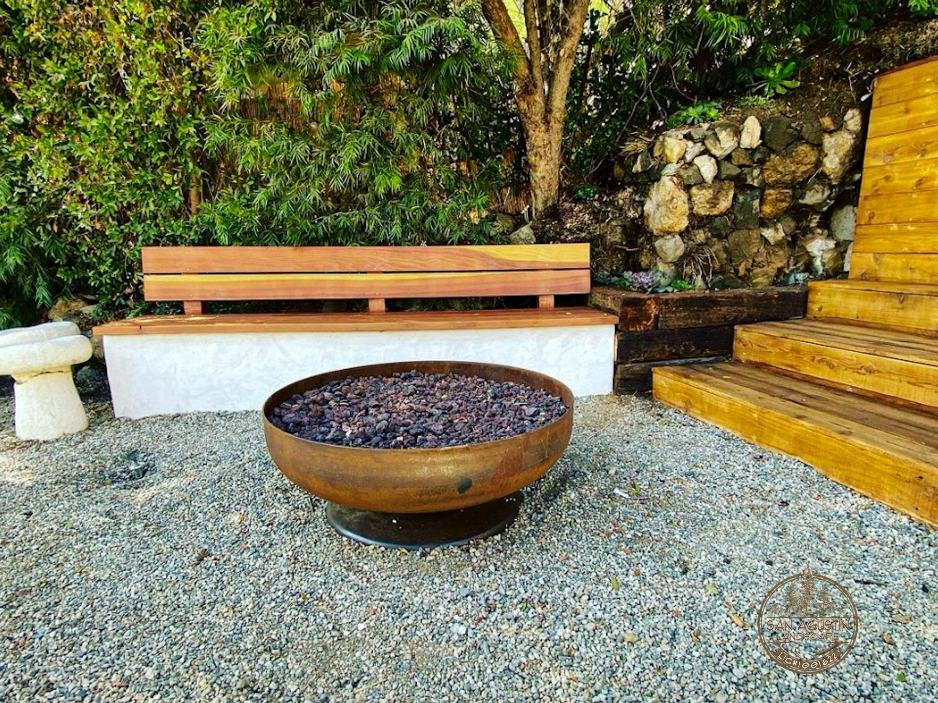 A fire pit with decorative rocks, a wooden bench, and steps in an outdoor setting.