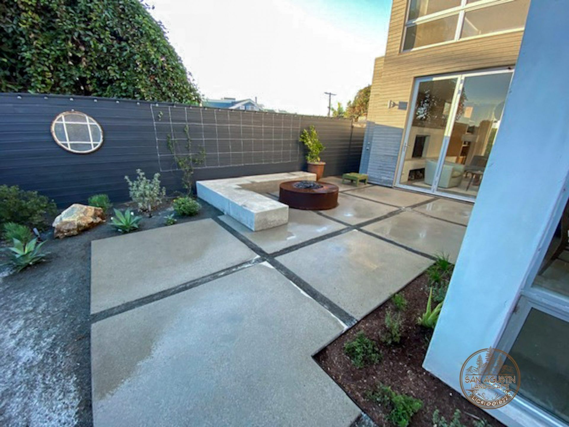 Modern backyard patio with concrete pavers, fire pit, and a grey fence.