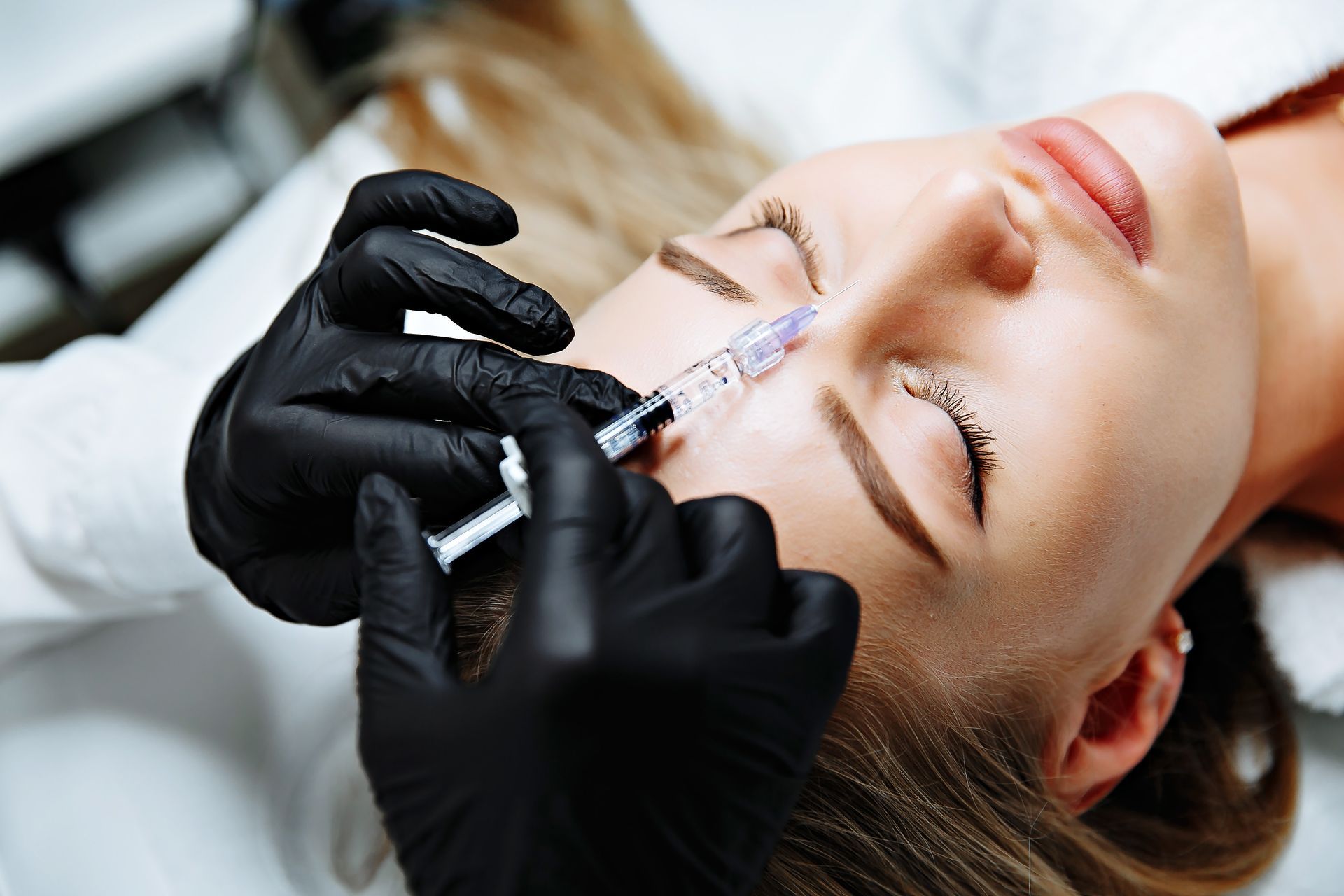 Person receiving an injection in the forehead; gloved hands, syringe visible, medical setting.