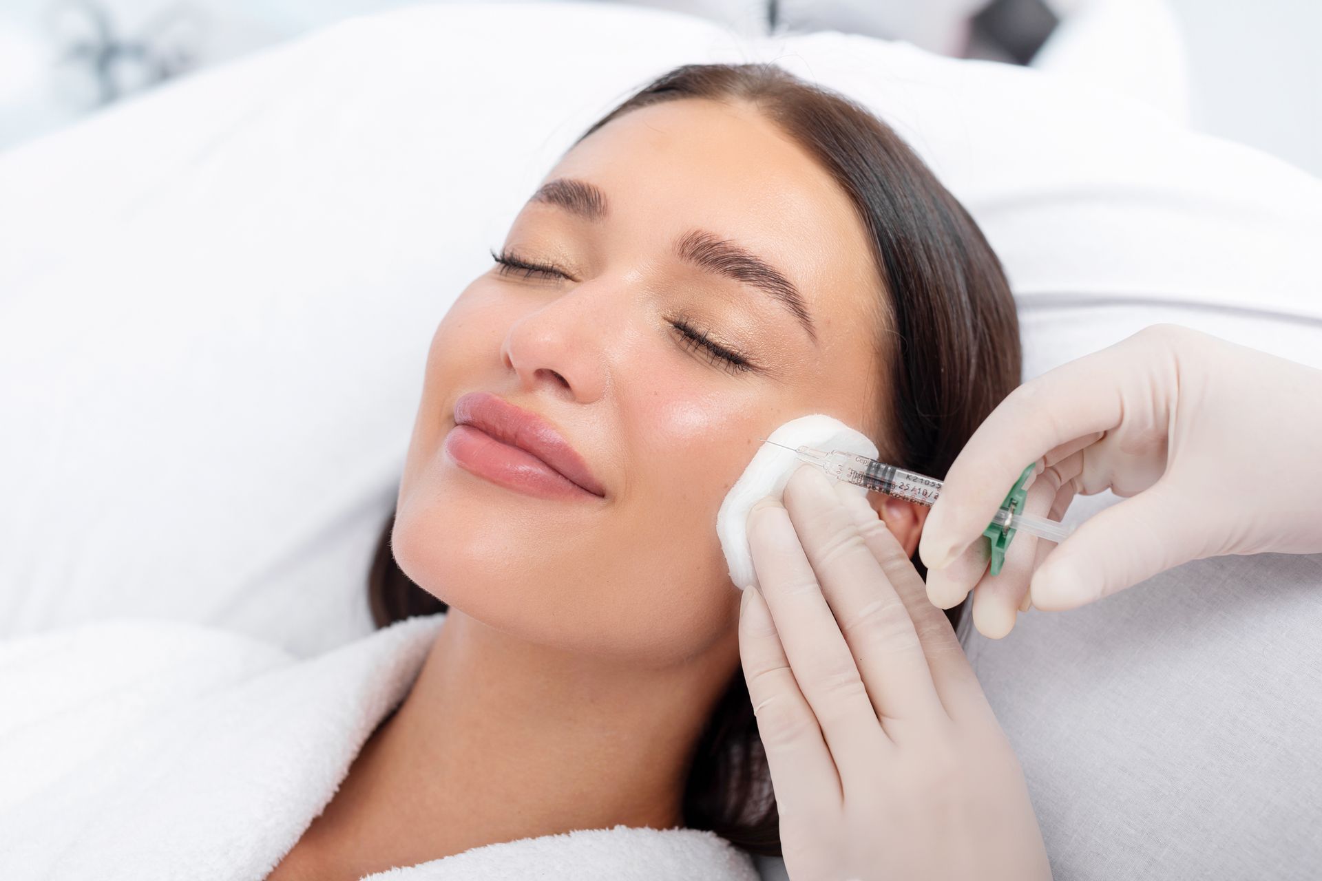 Woman receiving facial injection with gloved hands, indoors.