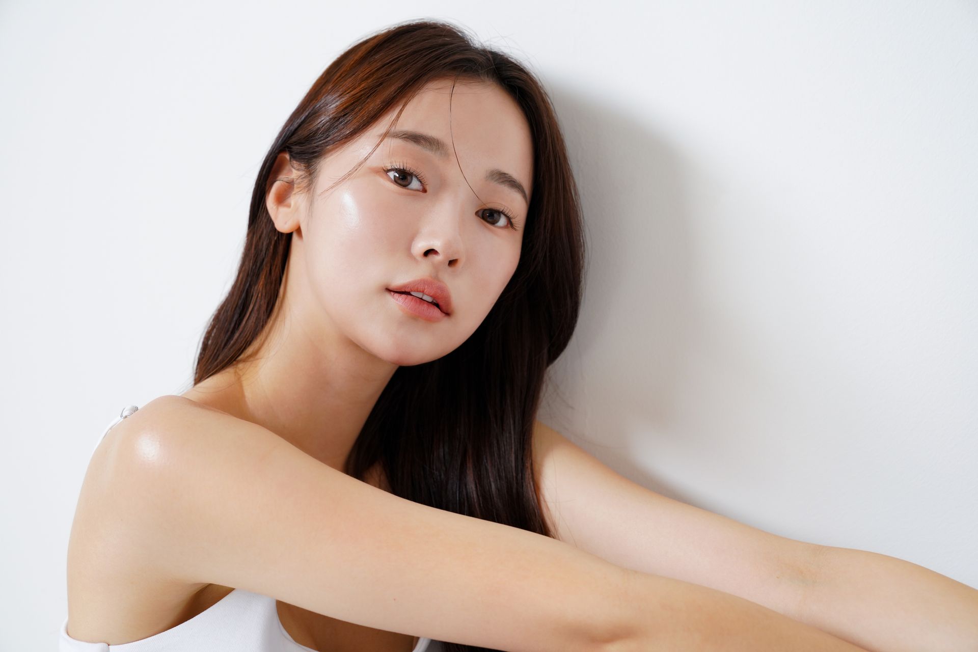 Woman with long brown hair, wearing a white top, looking at the camera. White background.