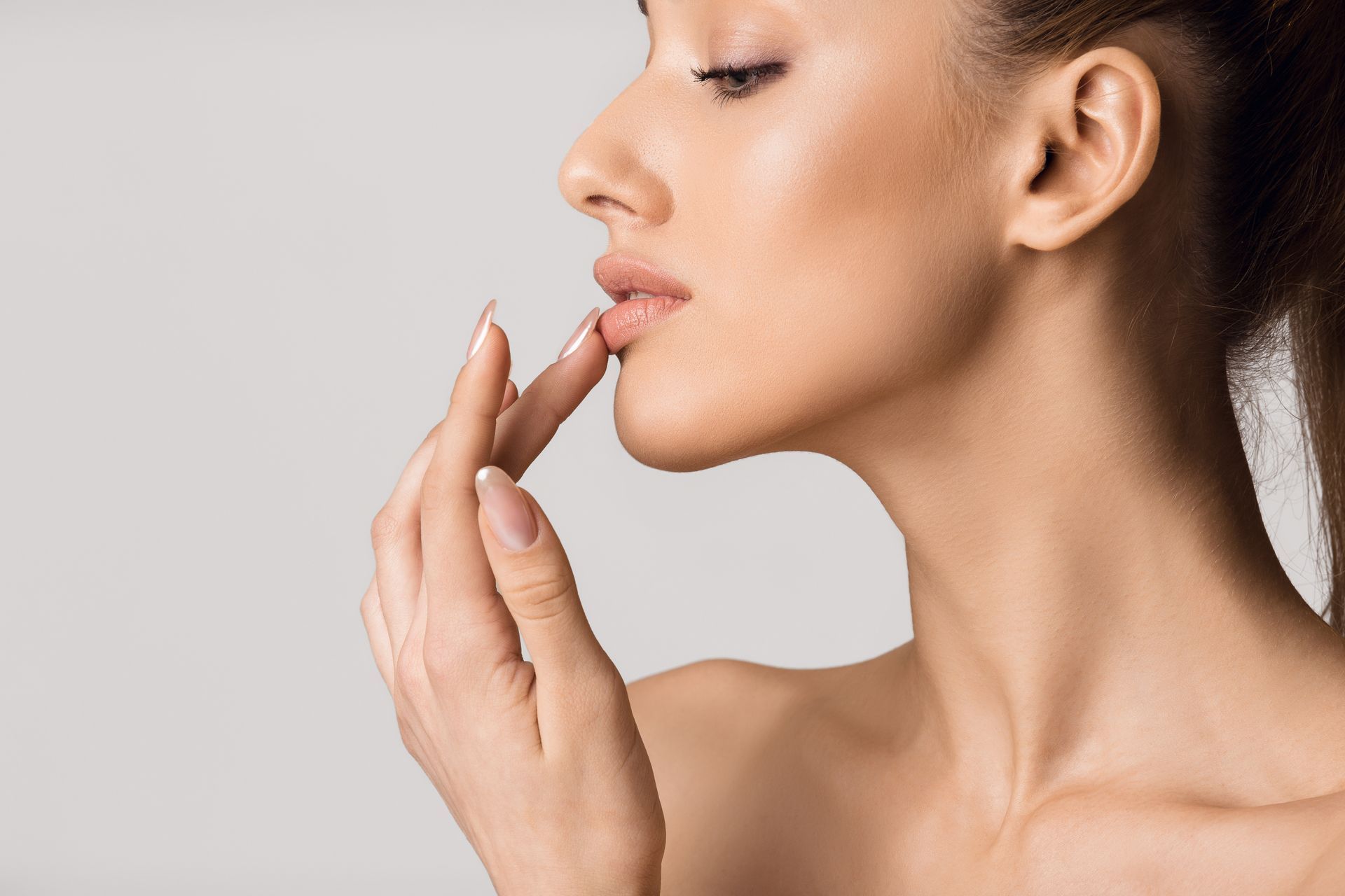 Woman touching her lip with index finger, neutral expression, light skin, bare shoulders.