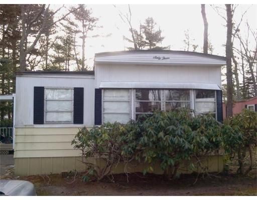 A white mobile home with black shutters is surrounded by trees