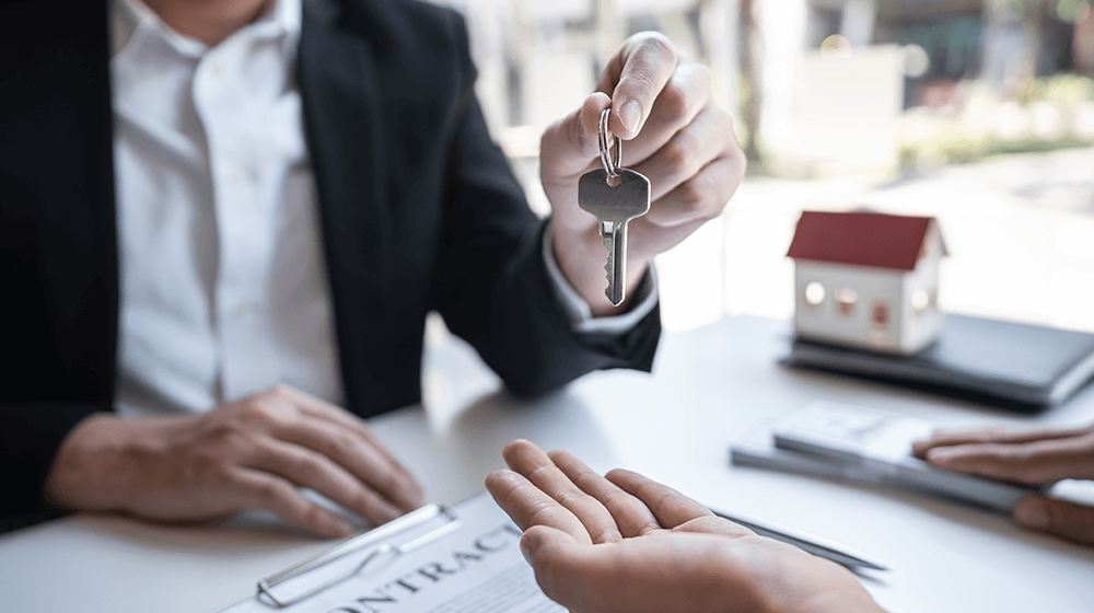 A man is giving a key to another man while sitting at a table.