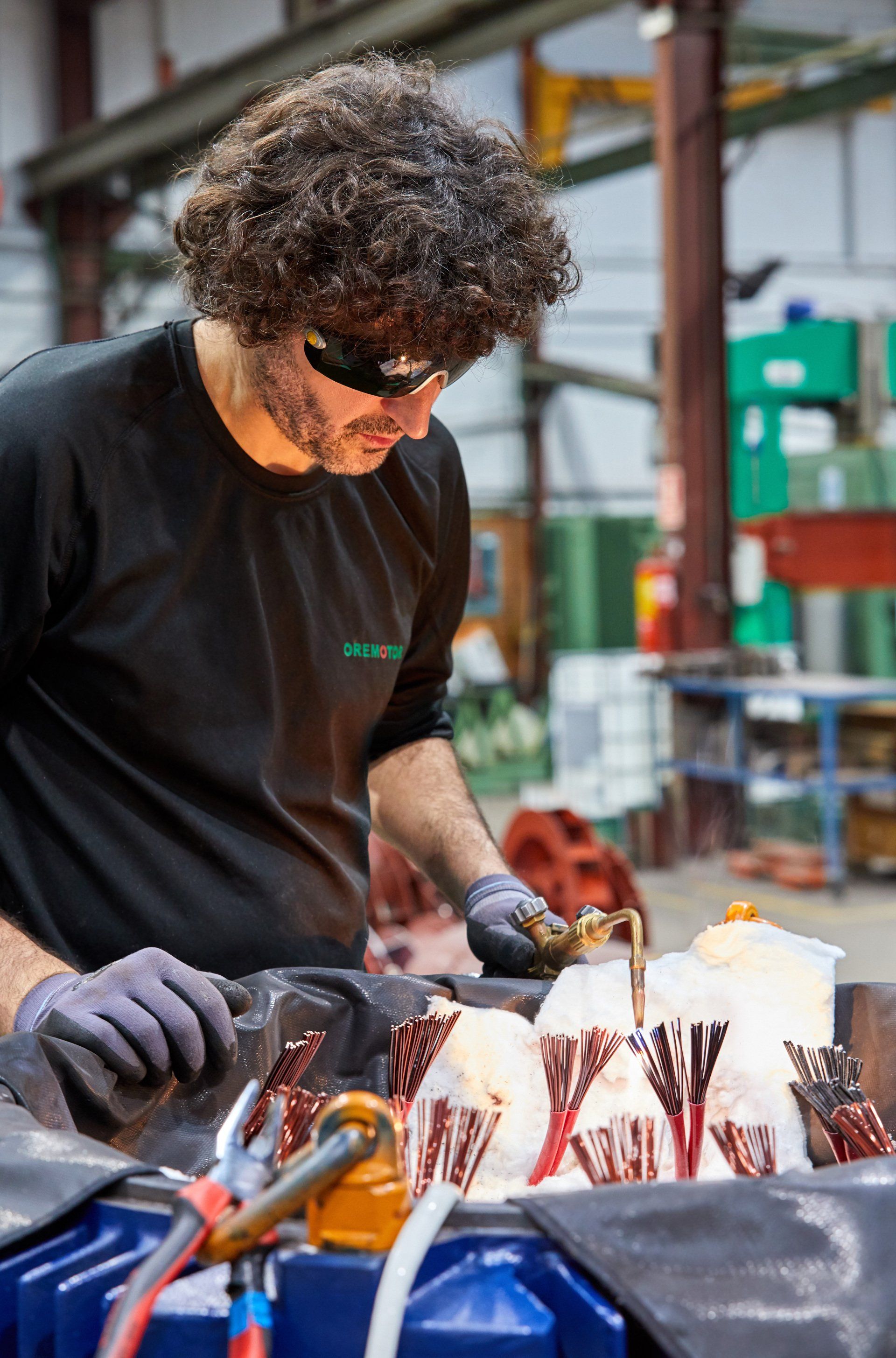 Hombre con cabello rizado y gafas de seguridad trabajando en un proyecto en una fábrica.