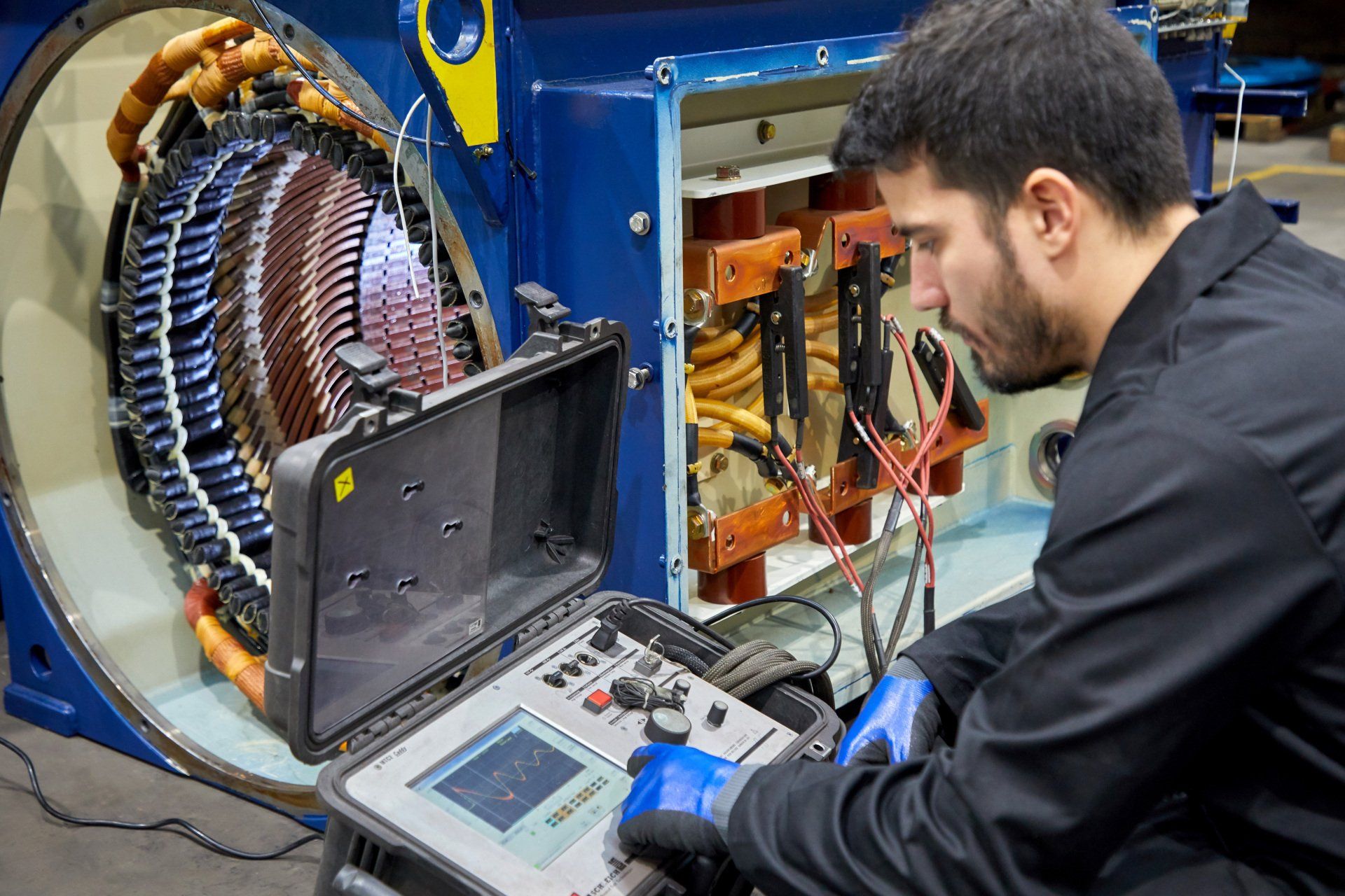 Un técnico inspecciona un gran motor industrial azul, utilizando un dispositivo de prueba.