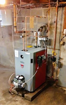 Gray and red boiler unit with pipes and gauges in a basement utility room