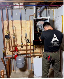 Man kneeling beside a green furnace, using a tool to inspect or repair its front components.